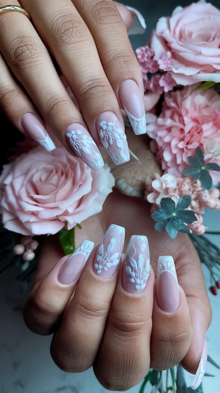Nails with white lace patterns on a pink and clear base, surrounded by flowers