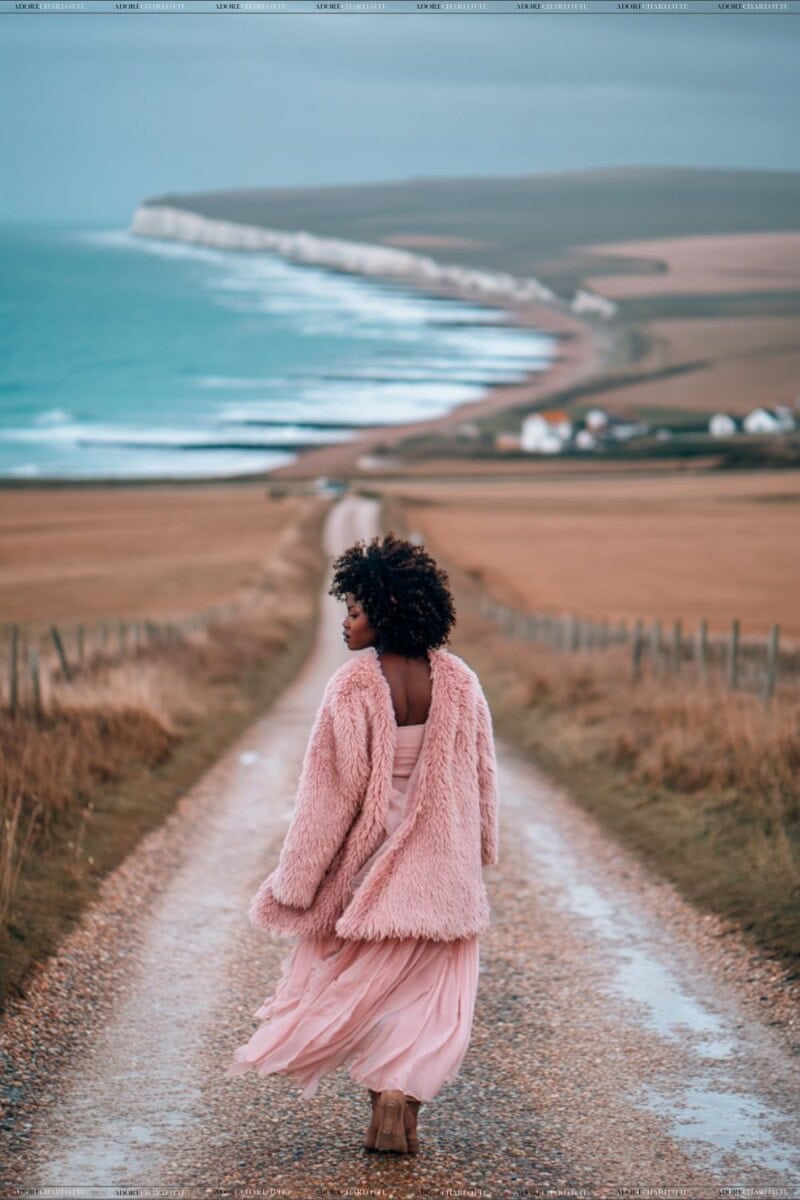 Woman walking toward a UK coastal beach on a dusty dirt path.